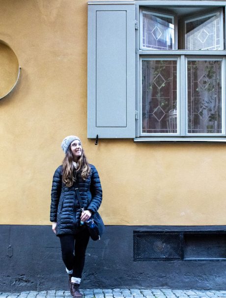 Katy standing in front of pale yellow wall with window in Stockholm, Sweden